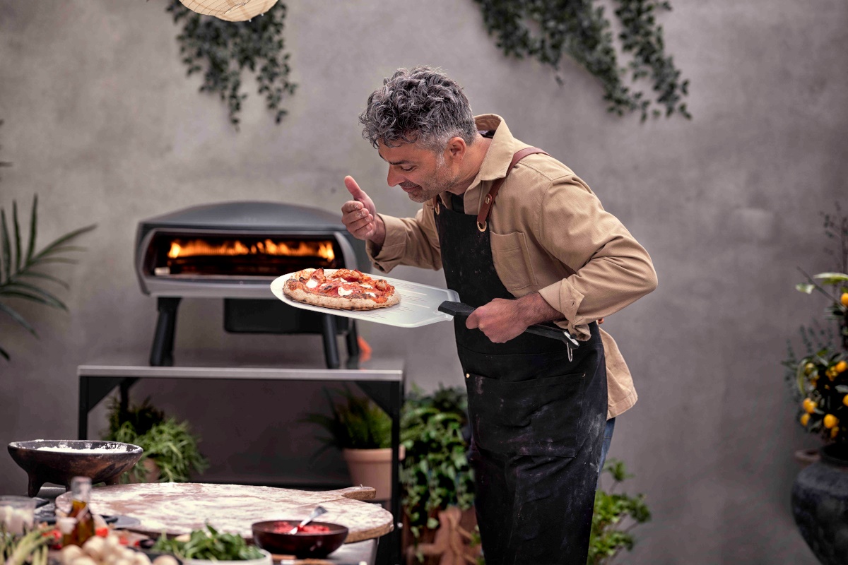 Mężczyzna pochyla się nad wyciągniętą z pieca pizzą na łopacie