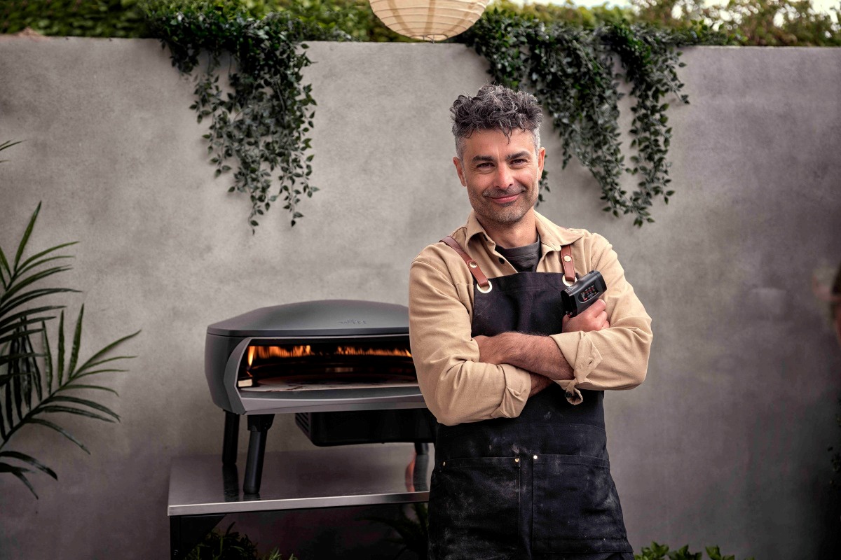 Uśmiechnięty pizzaiolo stoi przed odpalonym piecem Witt Etna Rotante